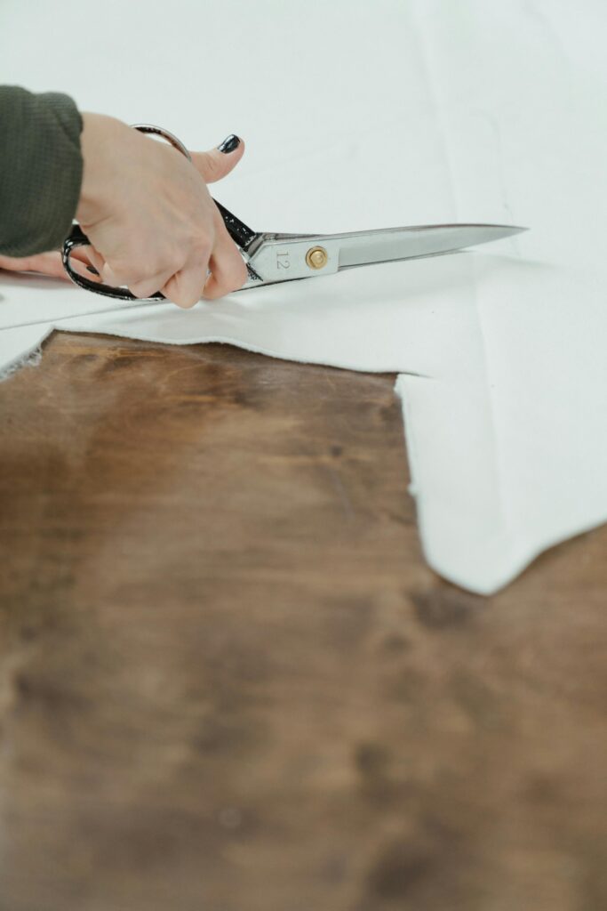 An artisan cuts white fabric on a wooden surface, emphasizing craftsmanship.