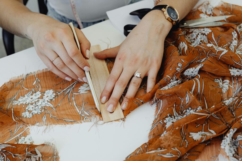 Close-up of hands expertly sewing fabric, showcasing the art of dressmaking in a workshop setting.